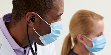 Közelkép egy klinikusról, a fülében fonendoszkóppal
