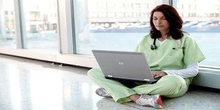 Klinikus ül a padlón, laptopot olvas
