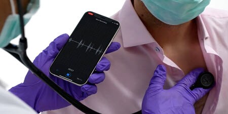 Laptopot használó klinikus, aki a laptopján nézi a valós idejű távgyógyászati auszkultációs videót
